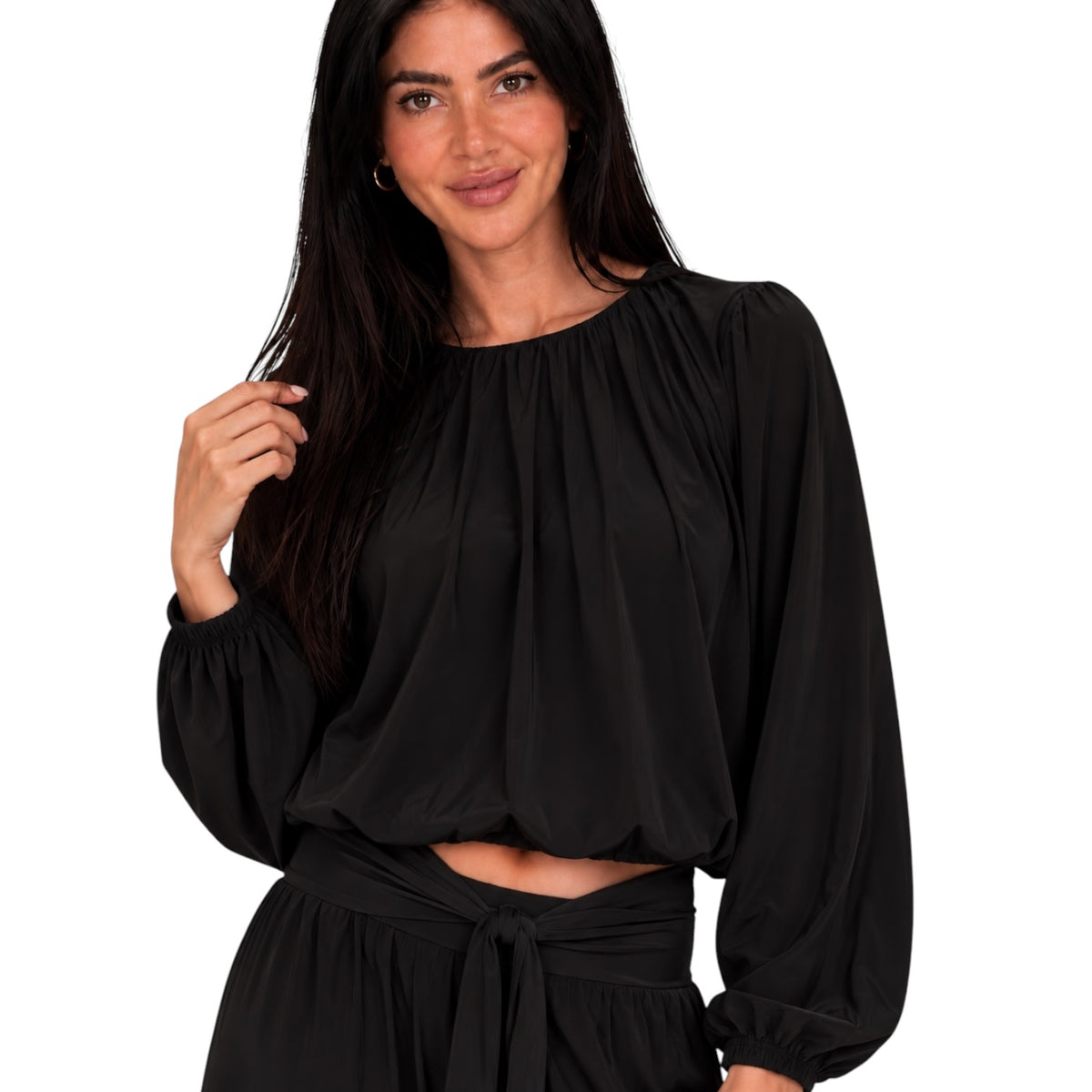 A woman wearing a black long-sleeve blouse with a gathered, balloon-style neckline and voluminous sleeves, paired with a matching black skirt, against a plain white background.