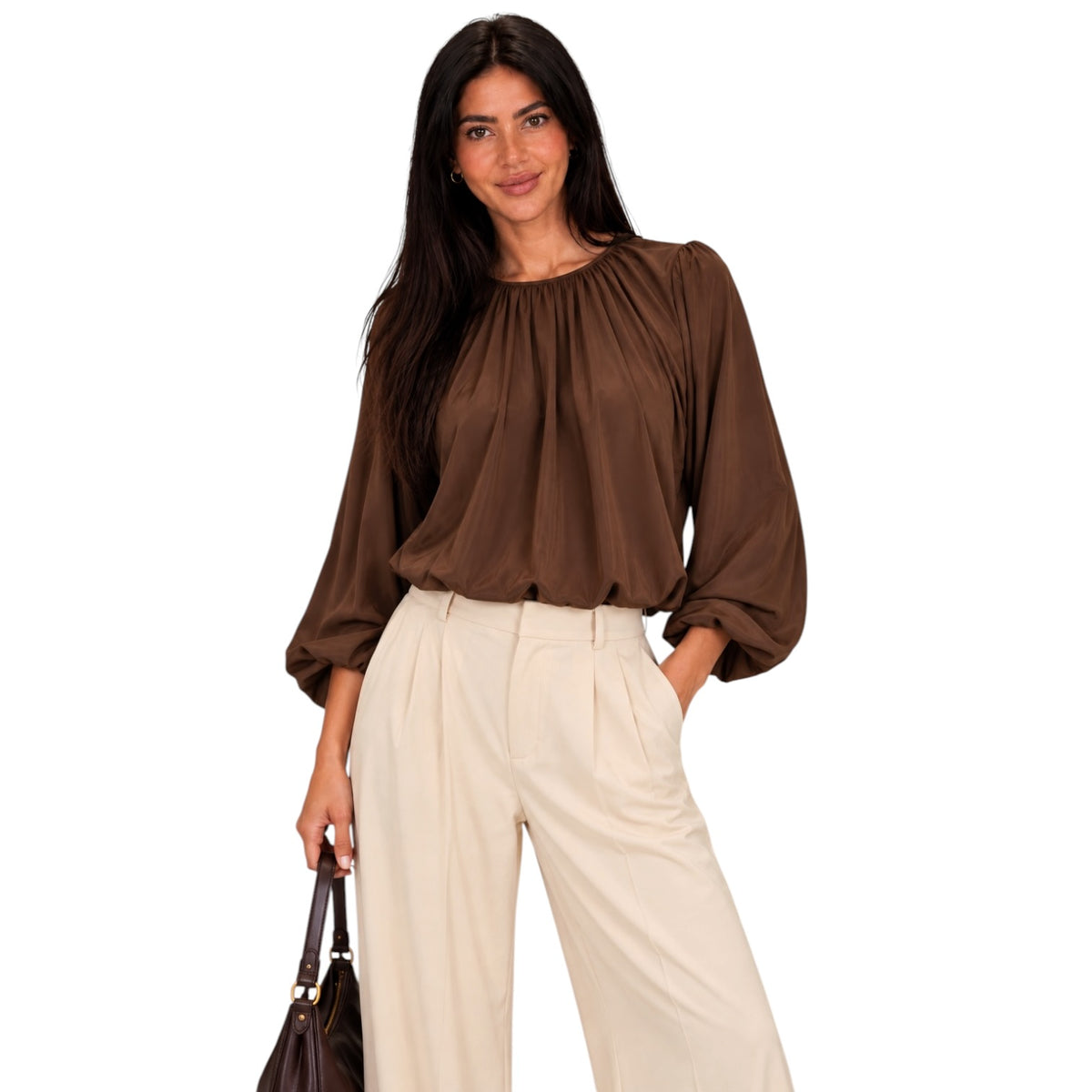 A woman modeling a brown long-sleeve blouse with a gathered neckline and pleated details, paired with cream wide-leg trousers, against a plain white background.