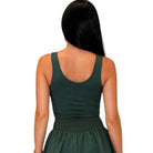 A woman viewed from the back wearing a dark green sleeveless dress with a scoop neckline and a gathered waist, against a plain white background.