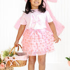 Young girl in a pink outfit with a large bow, holding a basket of flowers on a white background