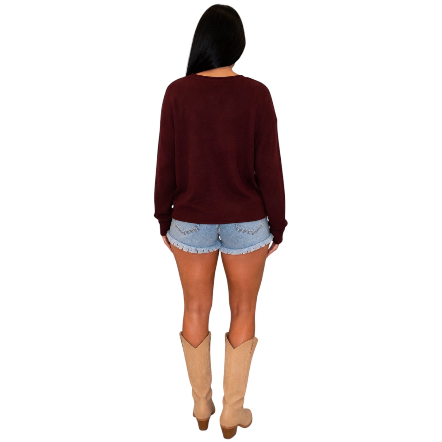 A woman shown from the back wearing a dark burgundy long-sleeve knit sweater, light blue denim shorts, and beige cowboy boots, set against a plain white background.