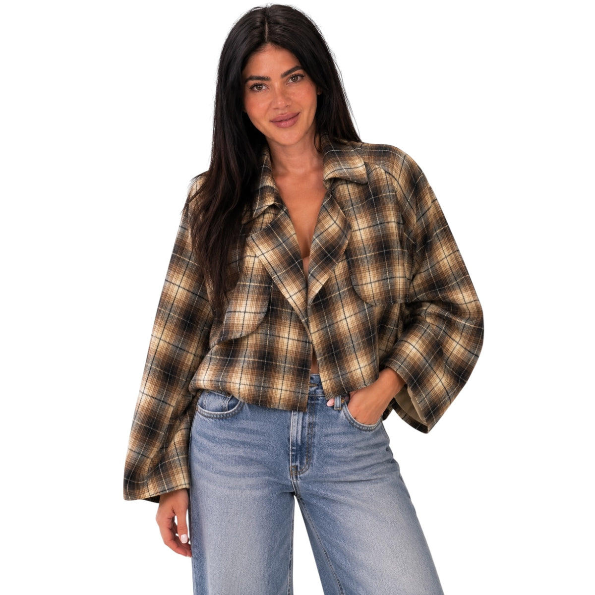 A woman modeling a cropped, long-sleeve plaid button-up shirt in brown, beige, and black, paired with light-wash blue jeans against a solid white background.