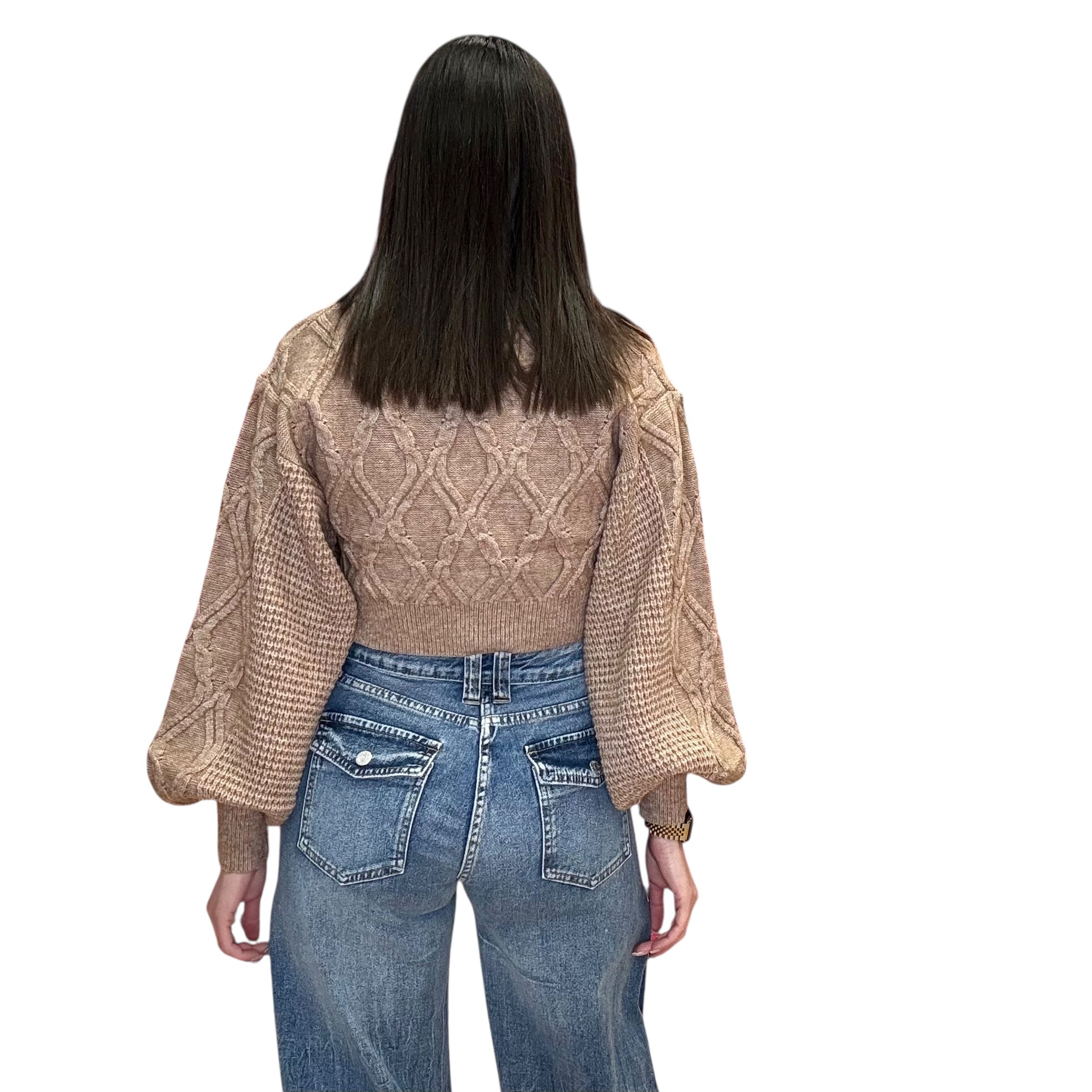 Person wearing a beige cable knit sweater and blue jeans on a white background