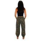 A woman viewed from behind wearing loose camouflage cargo pants, a black sleeveless crop top, and brown shoes against a plain white background.
