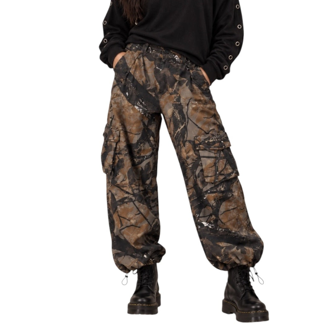 A woman modeling a black off-the-shoulder long-sleeve top with metal eyelets and brown camouflage cargo pants, paired with black combat boots, against a plain white background.