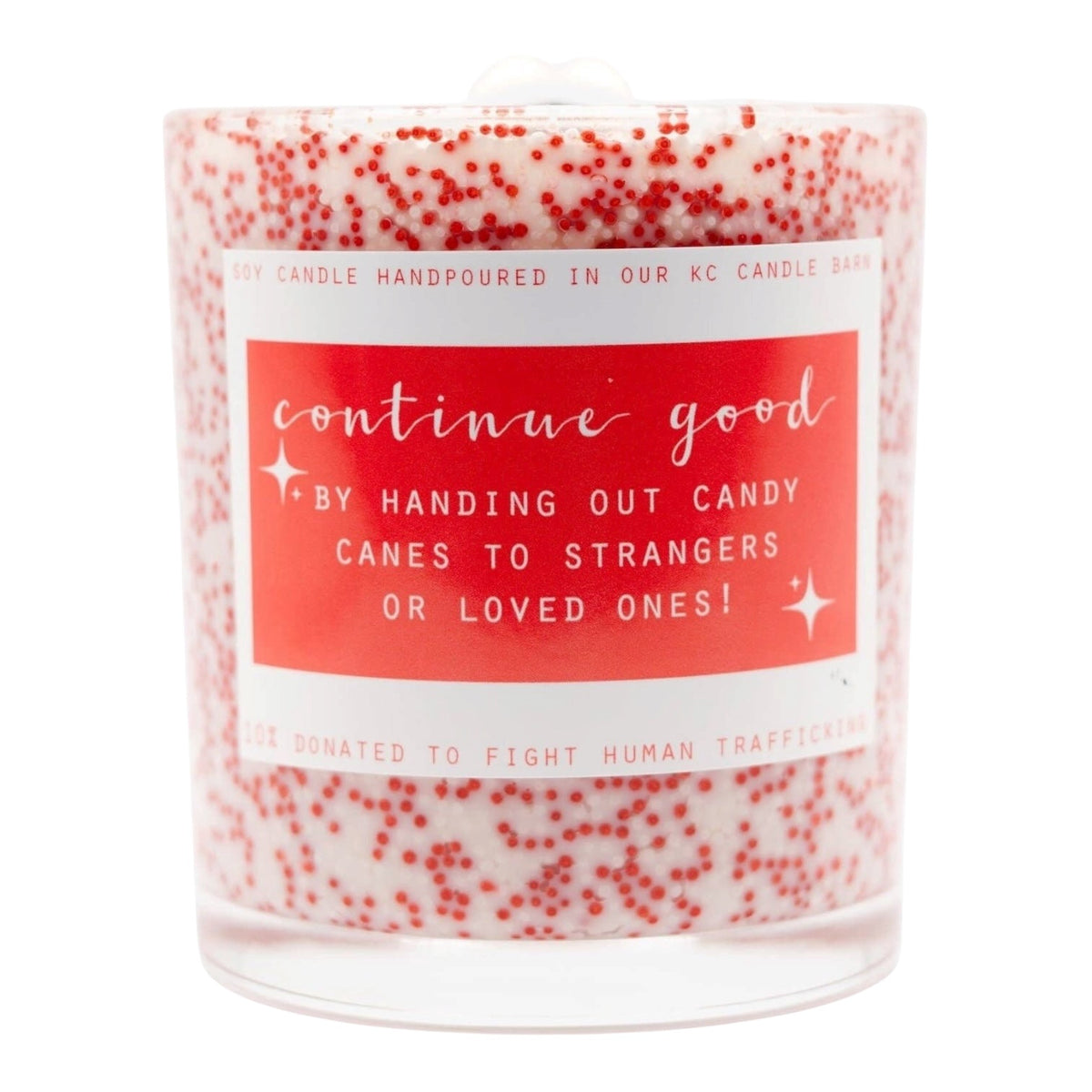 A hand-poured soy candle in a clear glass jar with a white wax base and red speckles, featuring a coral-red label with white text that reads 'continue good BY HANDING OUT CANDY CANES TO STRANGERS OR LOVED ONES!'.