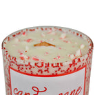 A close-up of a candle in a clear glass jar with red speckled wax and candy cane pieces on top, featuring a white label with red script text on a white background.