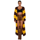 Woman wearing a long brown and yellow striped cardigan with a black top and brown leather shorts on a white background.