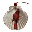 A decorative hanging ornament shaped like a white scallop shell with a red cardinal bird printed or painted across the center, topped with a red beaded loop and natural twine string.