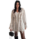 Woman wearing a beige ruffled romper holding a black handbag on a white background