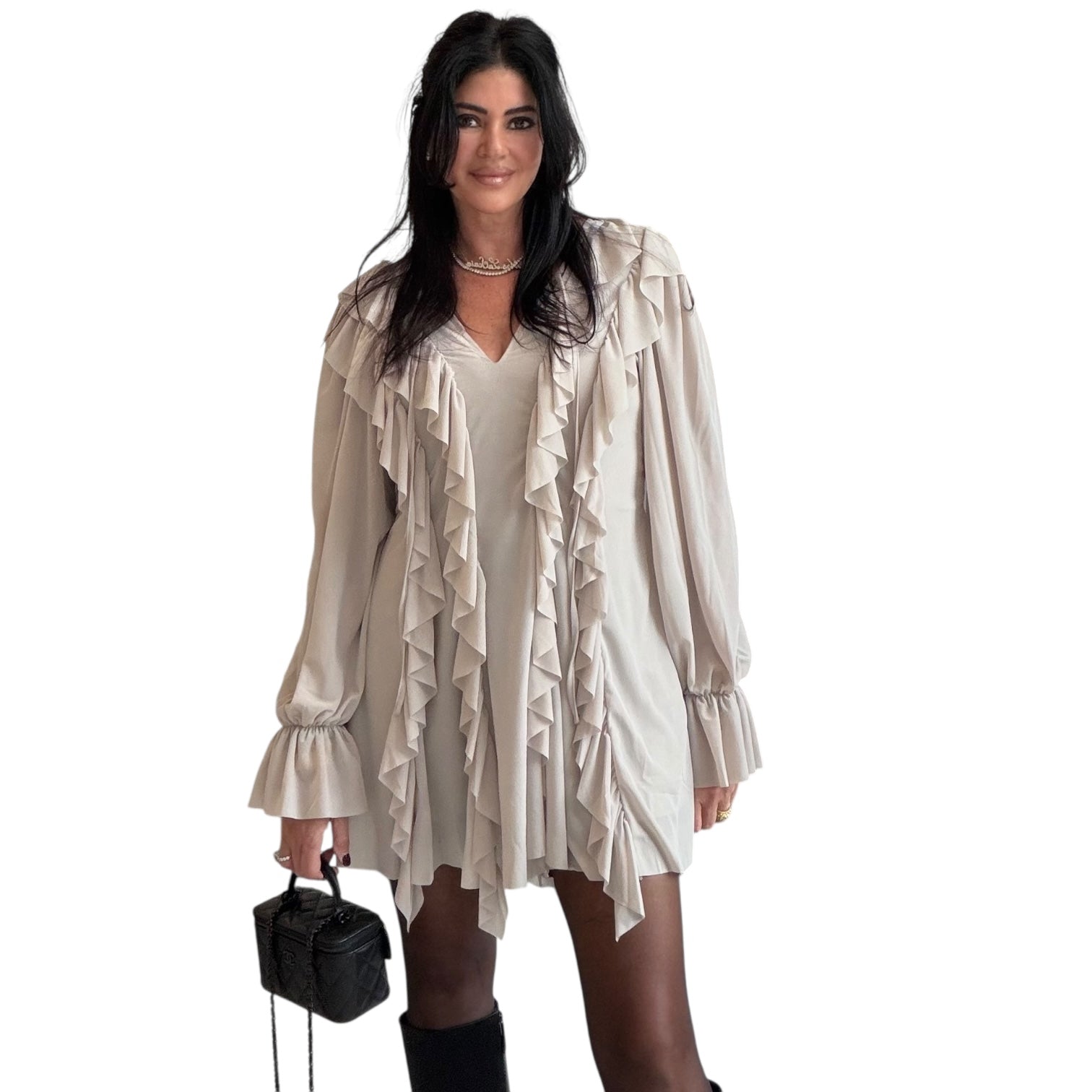 Woman wearing a beige ruffled romper holding a black handbag on a white background