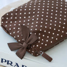 A brown nylon pouch with white polka dots, featuring a matching brown ribbon bow and a zip closure with a small brown pull tab, resting on a white surface.