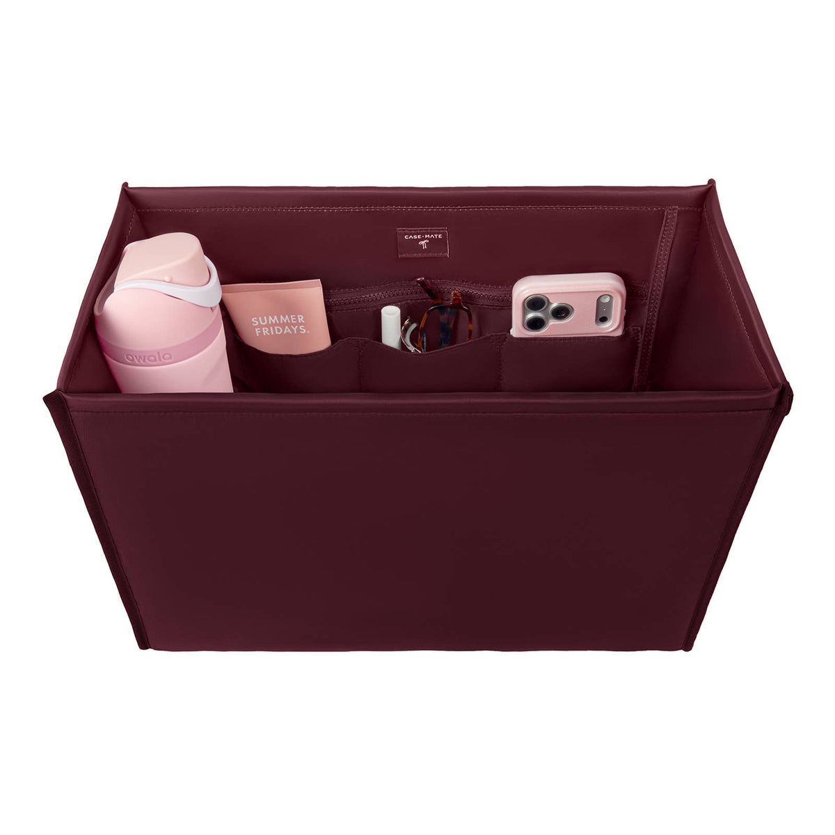A burgundy fabric organizer pouch shown from above, filled with travel accessories including a pink water bottle, a phone case, a small card holder, and a white item. The brand name 'Society6' is visible on the inside label and on the pink bottle.