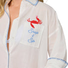 woman wearing white button down cover up with a crab with a wine glass coming out of the pocket that says "Snap & Sip" on white background.