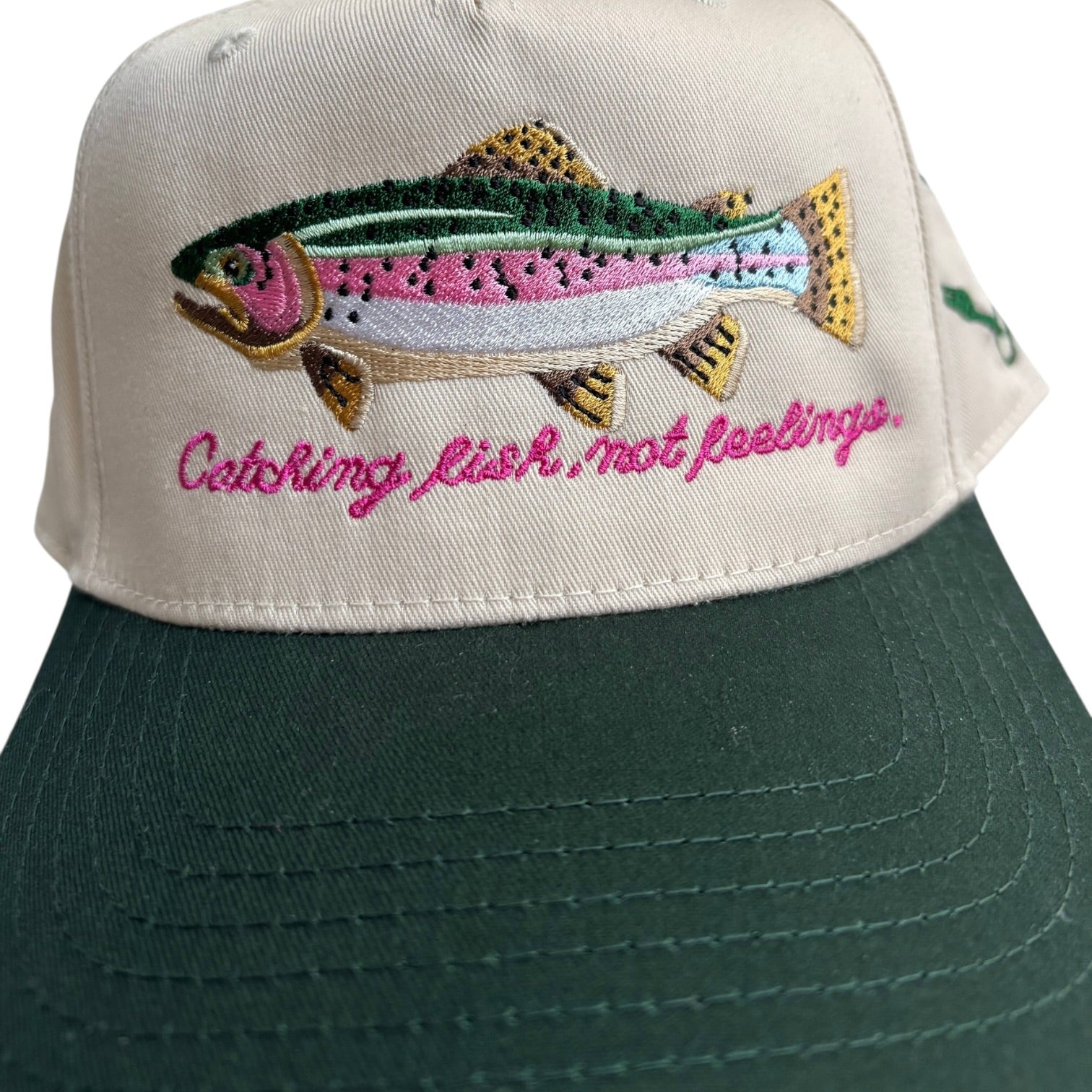 Green cap with embroidered fish and text on a beige background