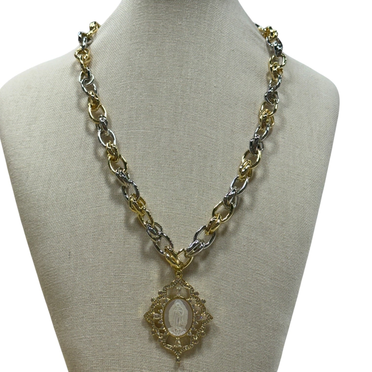 A two-tone gold and silver chain necklace with a central oval pendant, displayed on a beige fabric jewelry bust against a white background.