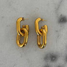 Gold chain-link earrings on a gray concrete surface