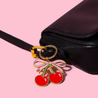 Black handbag with a cherry-themed keychain on a pink background