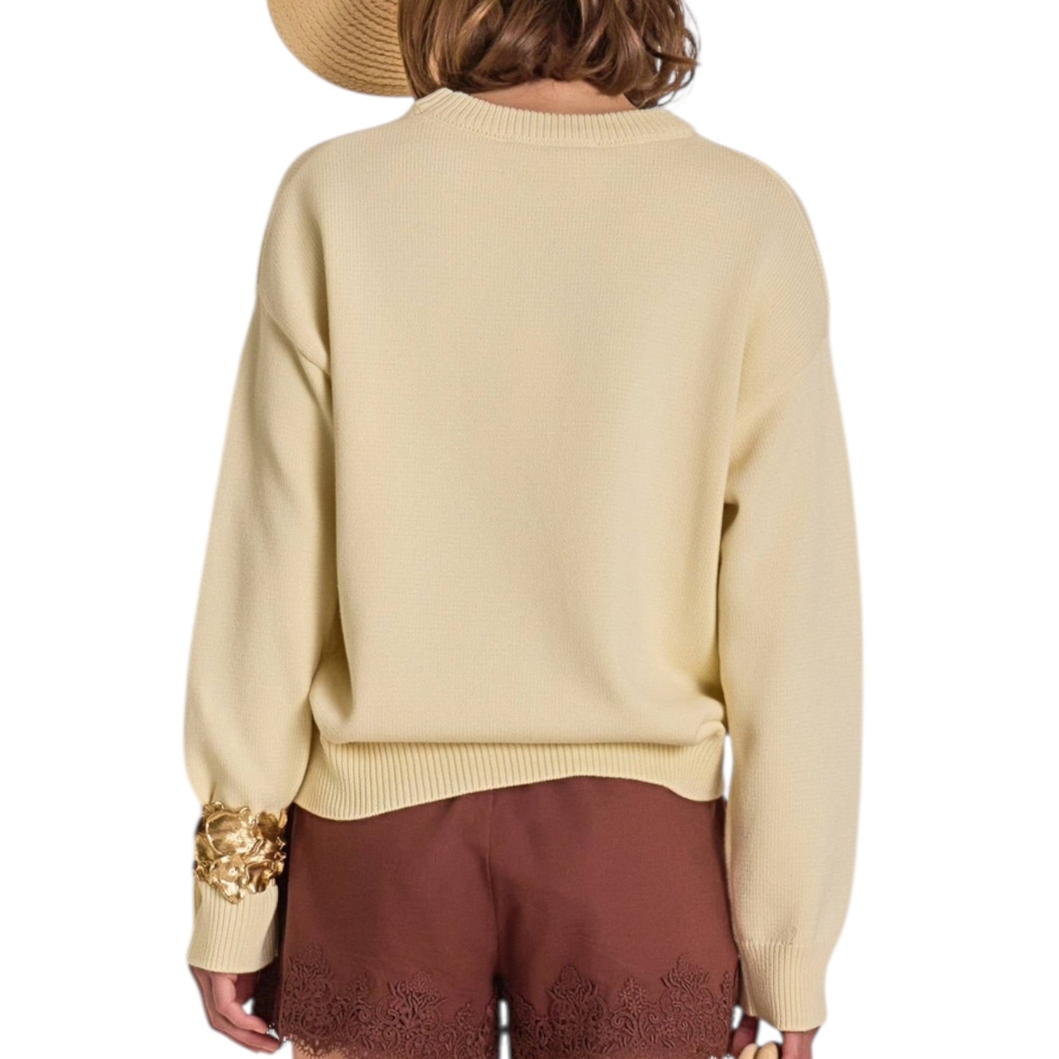 Person wearing a beige sweater with gold cuffs on a white background