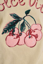 Embroidered pink cherries on a beige background with visible text.