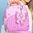 Pink backpack with butterfly charm held by a person against a light blue background