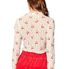 Woman wearing a lace top with cherry pattern and red pants on a white background