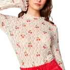 Woman wearing a lace top with cherry pattern and red pants on a white background