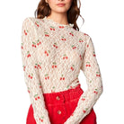Woman wearing a lace top with cherry pattern and red pants on a white background