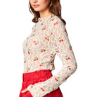 Woman wearing a white lace top with red cherry pattern and red pants on a white background