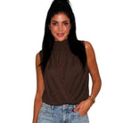 A woman wearing a sleeveless high-neck brown top and light-wash blue jeans, standing against a plain white background.