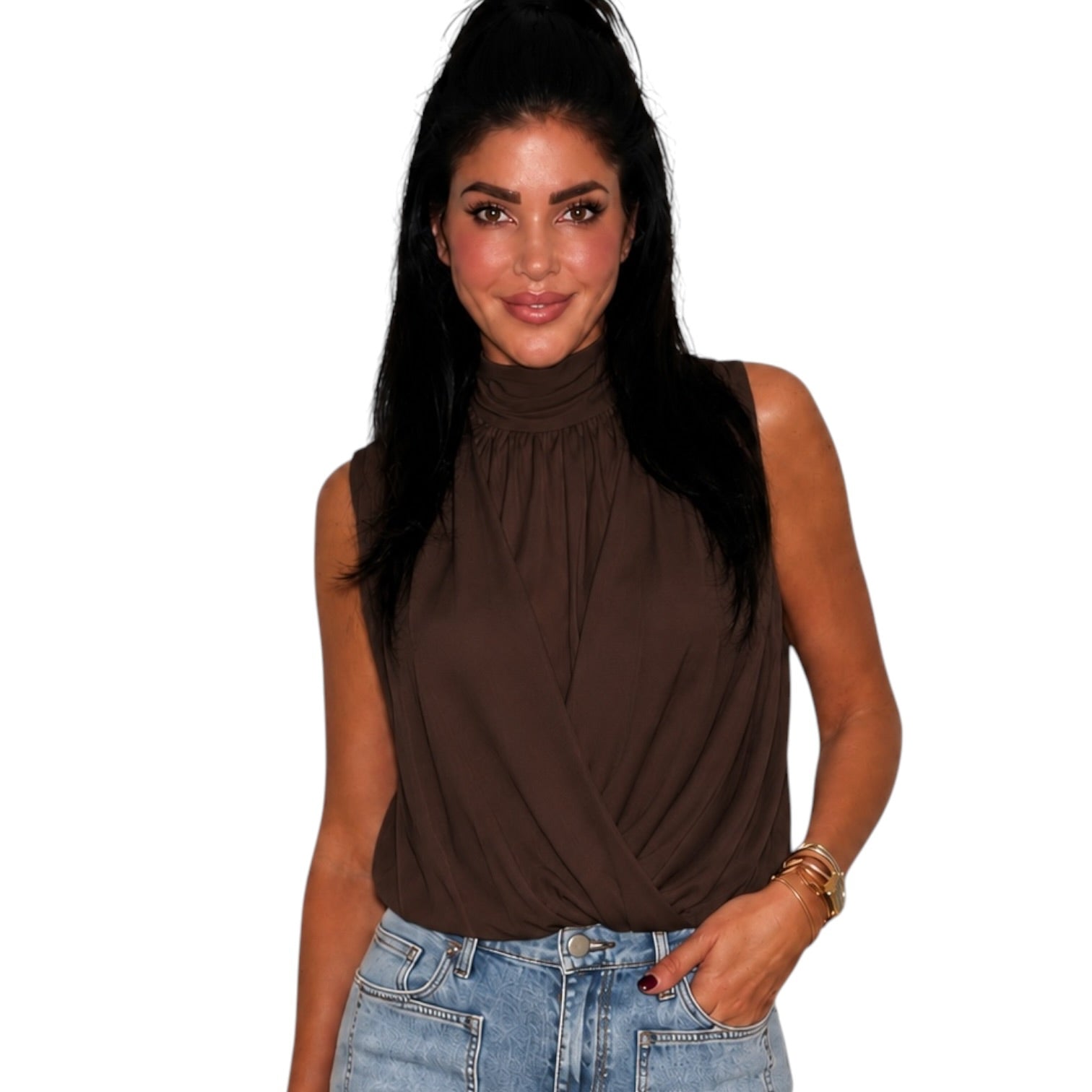 A woman wearing a sleeveless high-neck brown top and light-wash blue jeans, standing against a plain white background.
