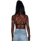 A woman viewed from the back wearing a sheer black lace long-sleeve crop top over light blue jeans, set against a plain white background.