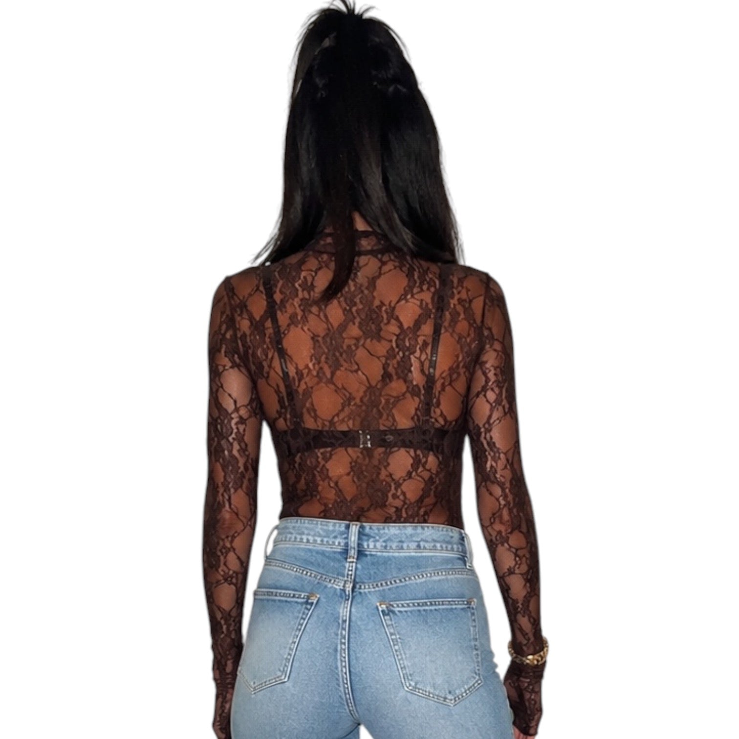 A woman viewed from the back wearing a sheer black lace long-sleeve crop top over light blue jeans, set against a plain white background.