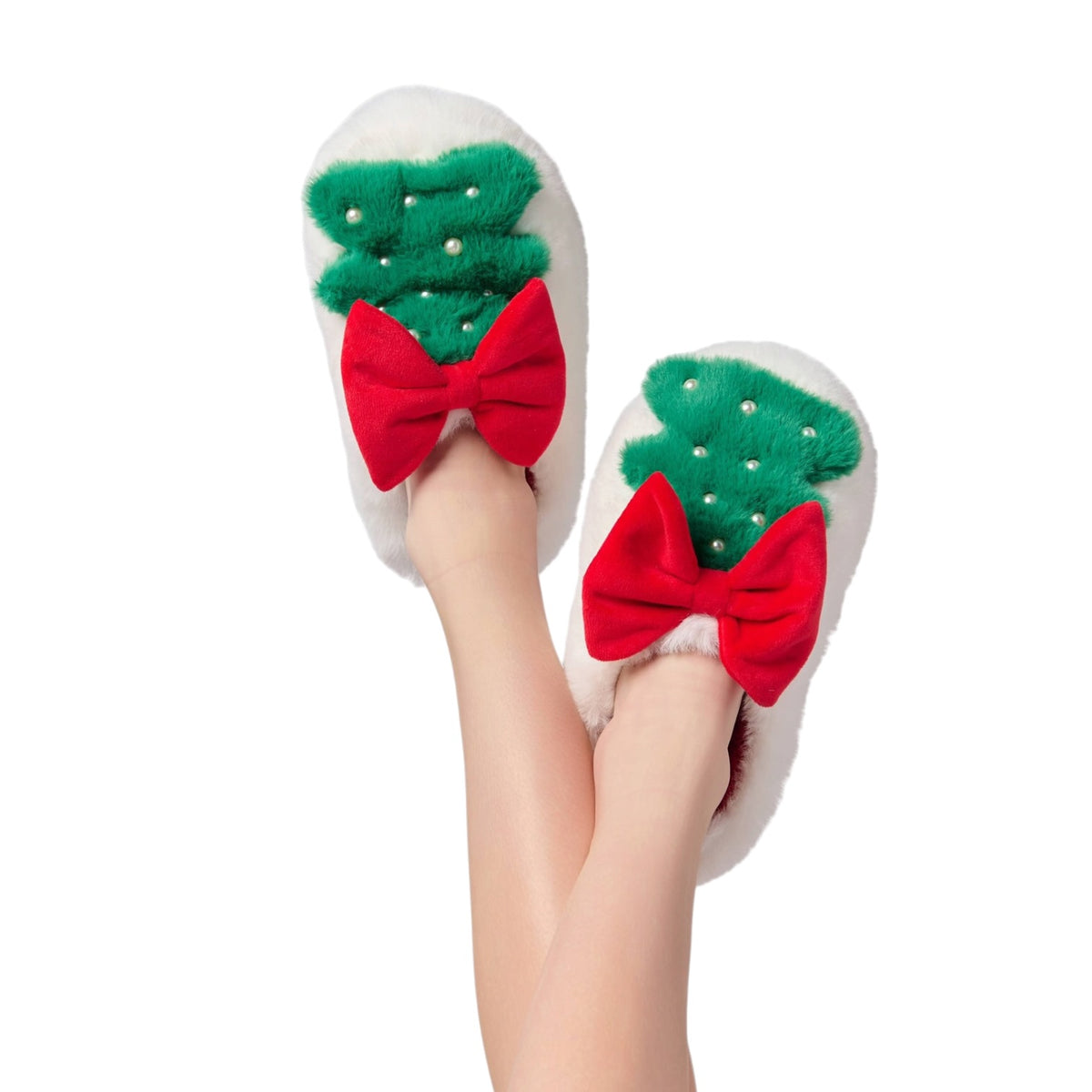 A pair of white fuzzy slippers with green holly designs and large red bows, shown on a person's feet against a plain white background.