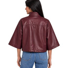 A woman shown from the back wearing a cropped, wide-sleeved faux leather jacket in a deep burgundy color, paired with blue jeans, against a plain white background.