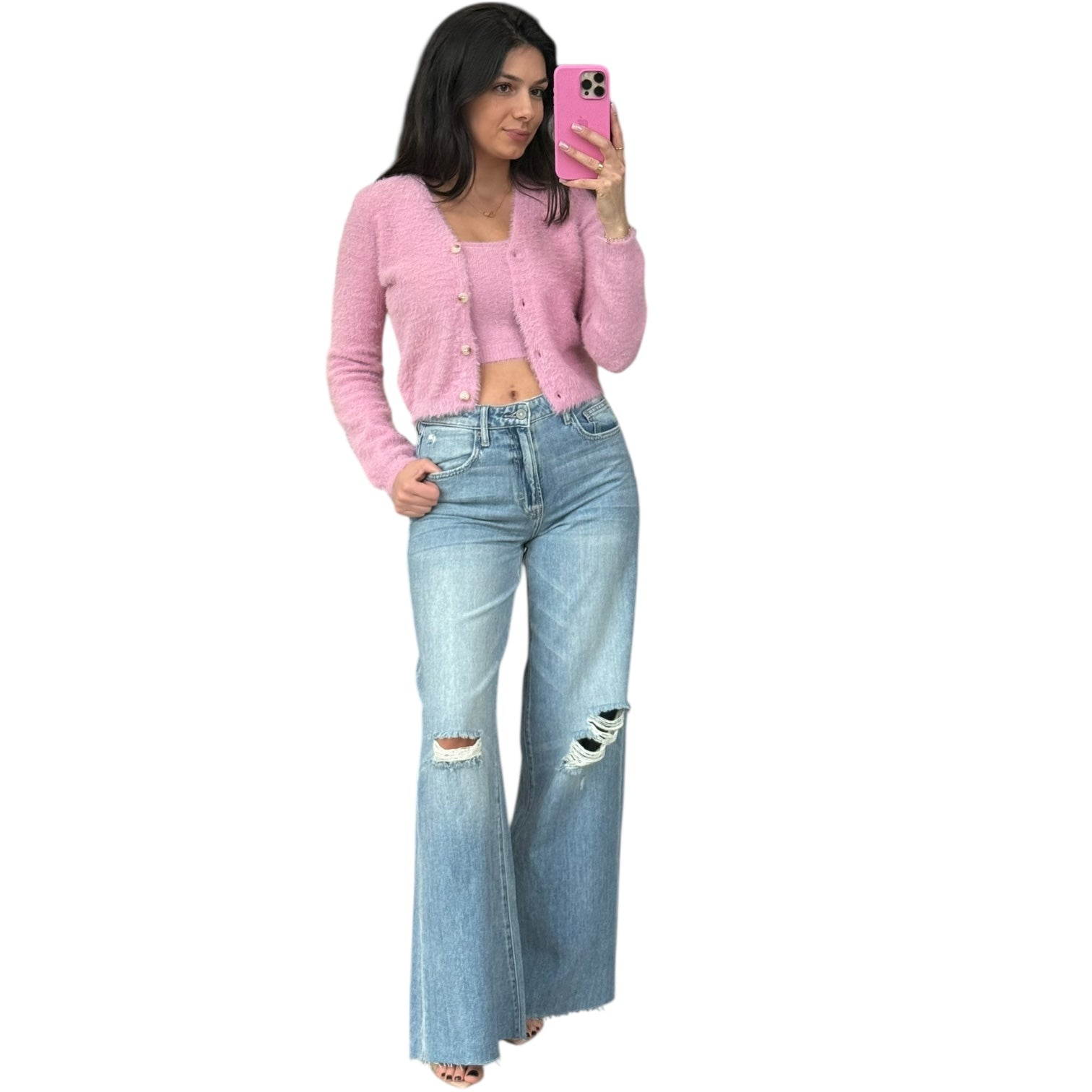 Woman wearing a pink cardigan and blue jeans, taking a selfie on a white background