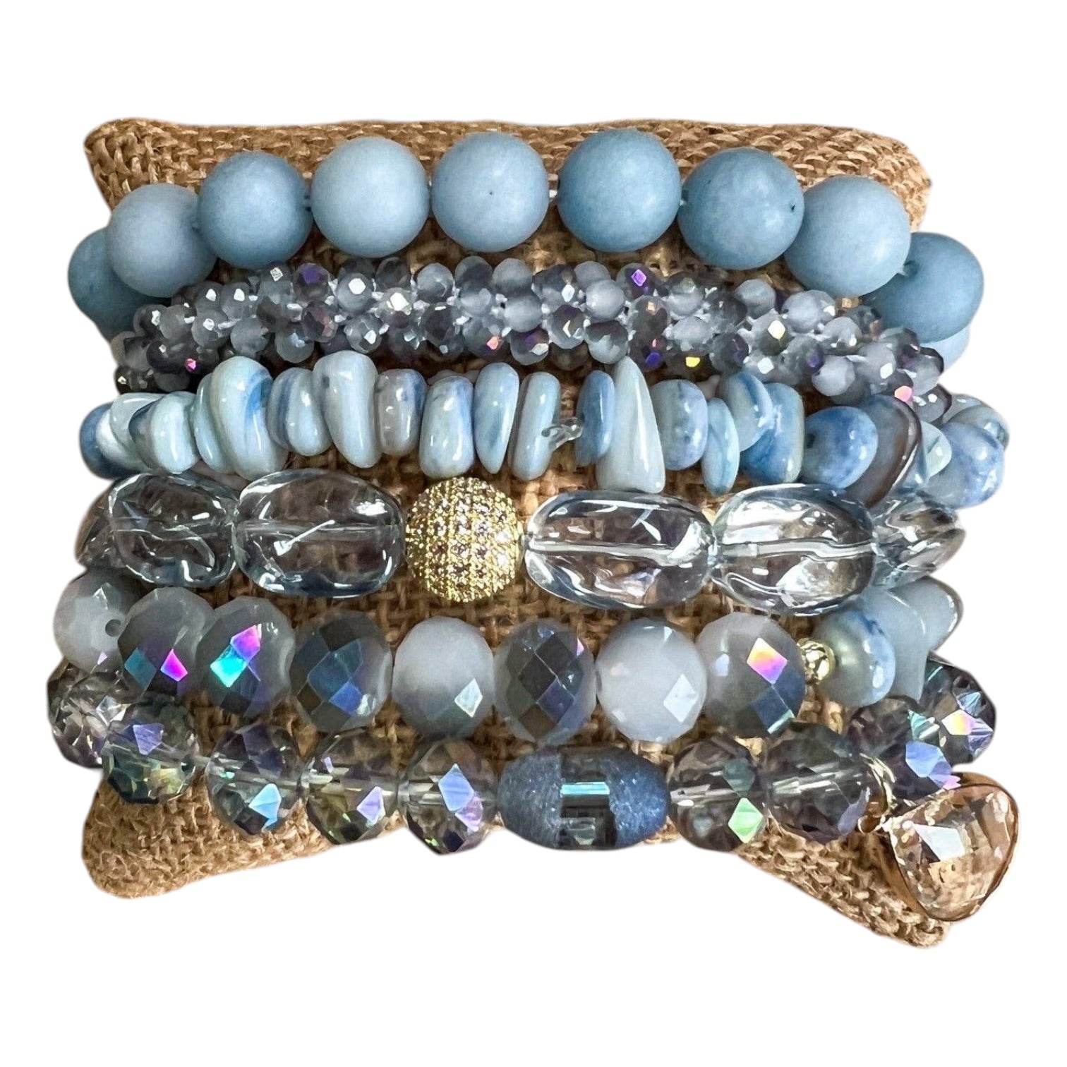 Stack of beaded bracelets with blue and clear stones on a textured surface