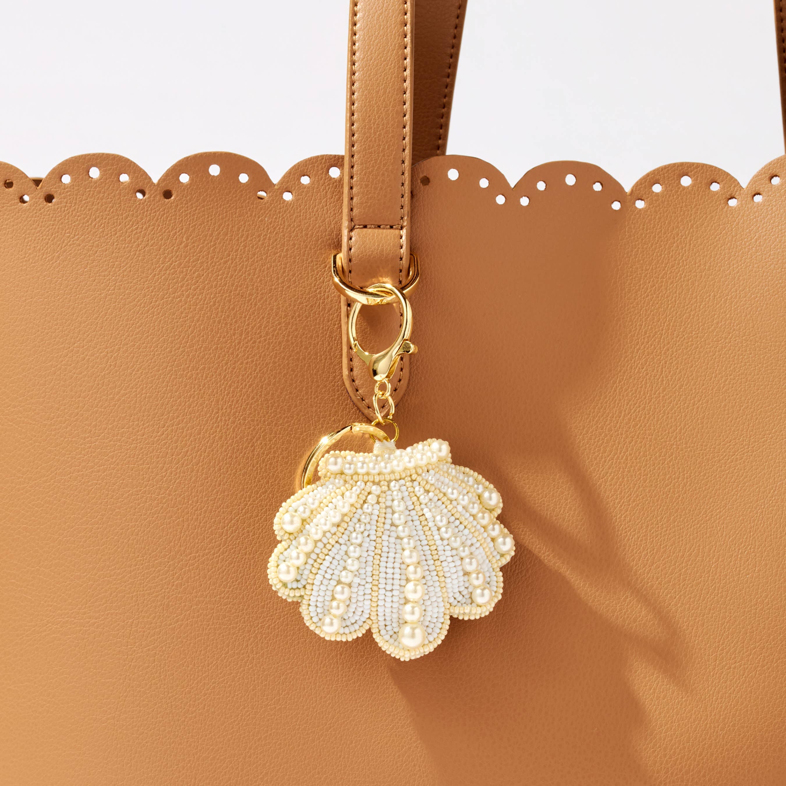 Gold and white shell-shaped keychain attached to a brown handbag.