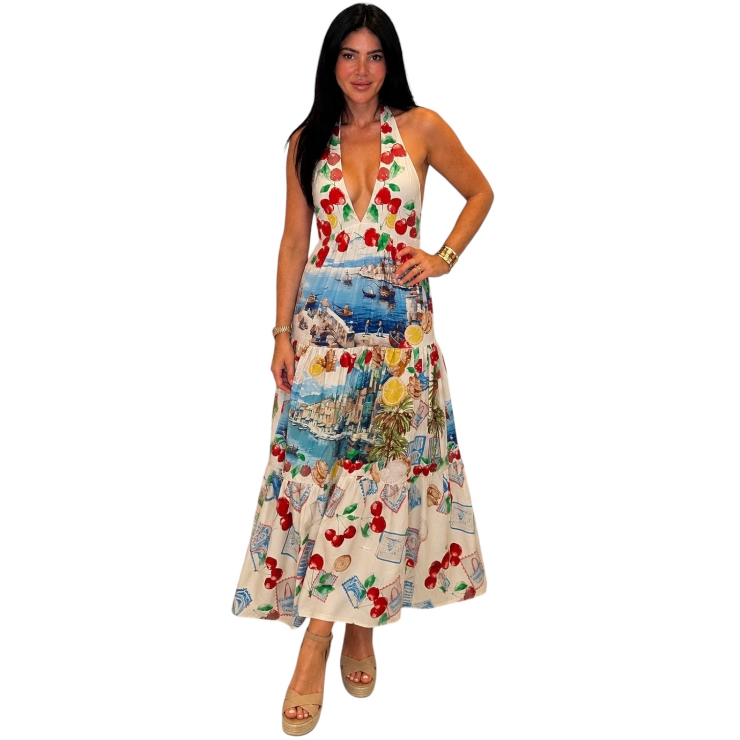 Woman wearing a colorful dress with a pattern of cherries and scenic designs on a white background