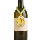 A green beaded wine bottle charm with a yellow accent bead and a decorative teardrop pendant featuring a lemon illustration and the text 'de Citron', shown hanging from a dark wine bottle against a white background.