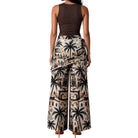 Woman wearing a sleeveless brown top and patterned wide-leg pants with palm tree design on a white background