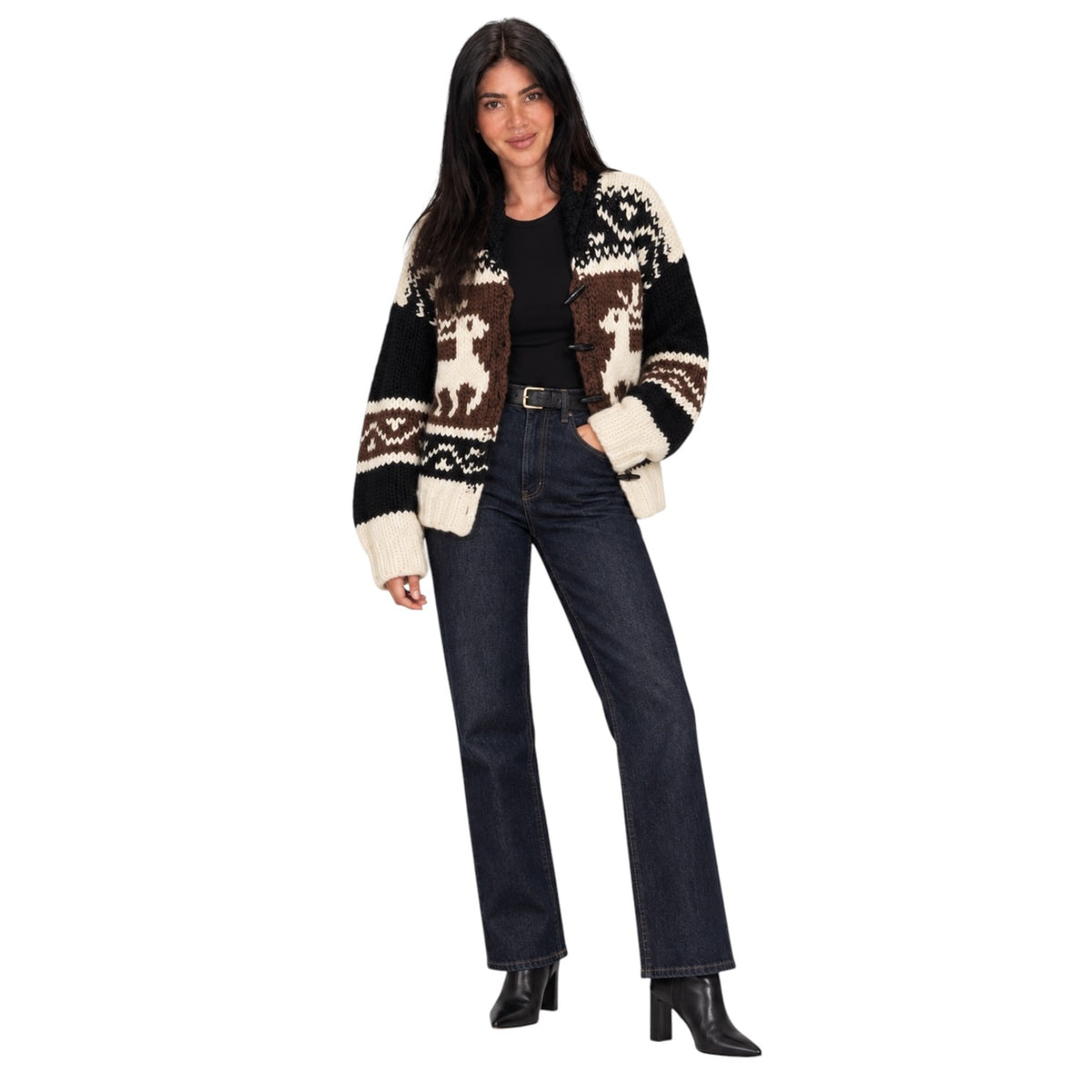 A woman modeling a black, brown, and cream knit cardigan with a Fair Isle pattern featuring reindeer motifs, paired with dark blue jeans and black ankle boots against a solid white background.