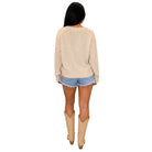 A woman shown from the back wearing a cream-colored knit sweater, denim shorts, and beige cowboy boots against a plain white background.