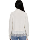 A woman viewed from the back wearing a cream-colored knit sweater with a lace hem overlay and light blue jeans, set against a plain white background.