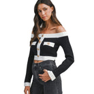 Woman wearing a black and white off-shoulder top with gold buttons on a white background