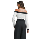 Woman wearing a white off-shoulder top with black trim and black pants on a white background