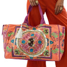 Colorful embroidered bag held by a person wearing orange pants on a white background