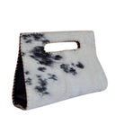 A small handbag made from black-and-white spotted cowhide with a cutout handle, shown on a plain white background.