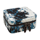 A square zippered jewelry box with a blue, black, and white cowhide pattern, featuring dark brown leather zipper pulls, shown on a plain white background.