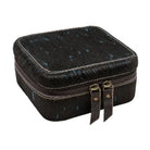 A square black hair-on-hide jewelry box with blue speckles, featuring light-colored stitching, a zippered closure, and two leather pull tabs with brass hardware, shown on a plain white background.
